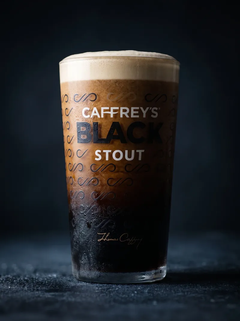 Caffrey's Black Stout pint with a dense creamy head on a dark background, commercial beer photography