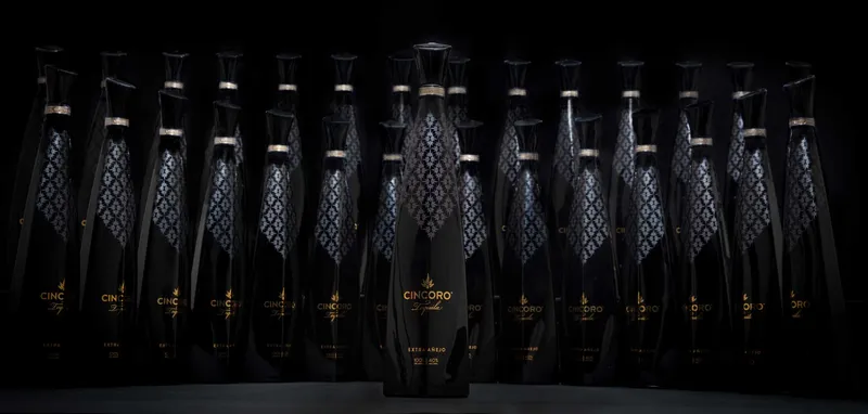 Cincoro Extra Añejo tequila bottle lit in front of rows of identical bottles fading into black.