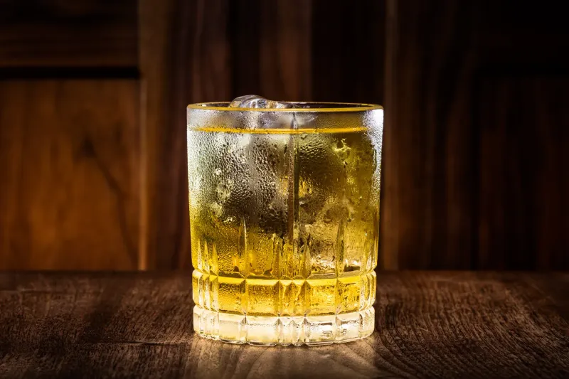 Whiskey highball over ice in a cut crystal rocks glass, condensation raised on the glass