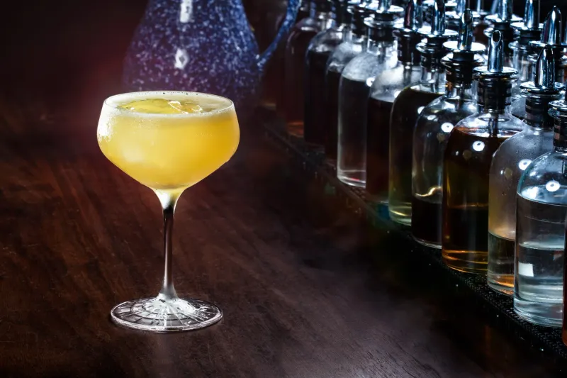Golden sour served up in a coupe on the Dead Rabbit bar, dasher bottles racked behind