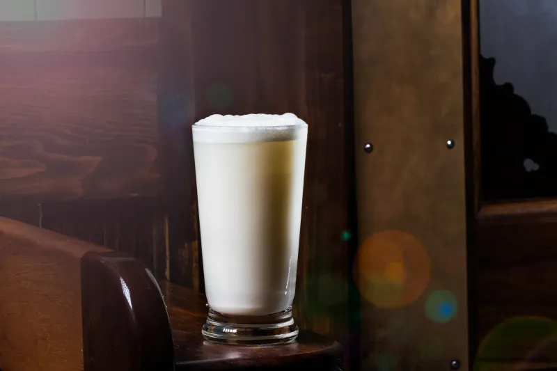 Fizz with a dense white foam cap in a tall glass against the Dead Rabbit wood panelling