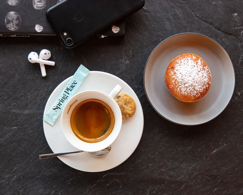 Overhead espresso at Spring Place with a sugar dusted bombolone, cookie, phone, and earbuds on slate