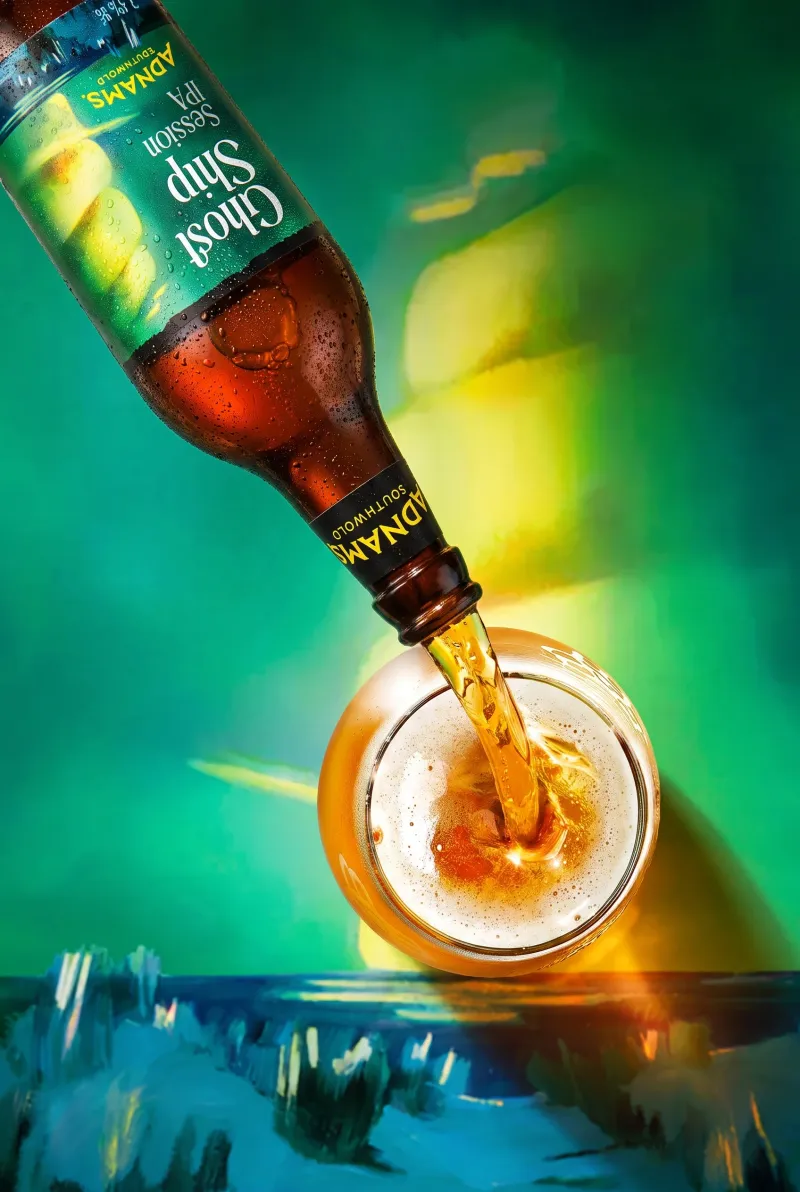 Adnams Ghost Ship Session IPA poured from the bottle into a glass against a green backdrop, commercial beer photography