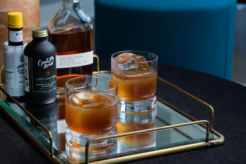 Owl's Brew salted caramel toddy served over large ice with bourbon and bitters on a mirrored bar tray