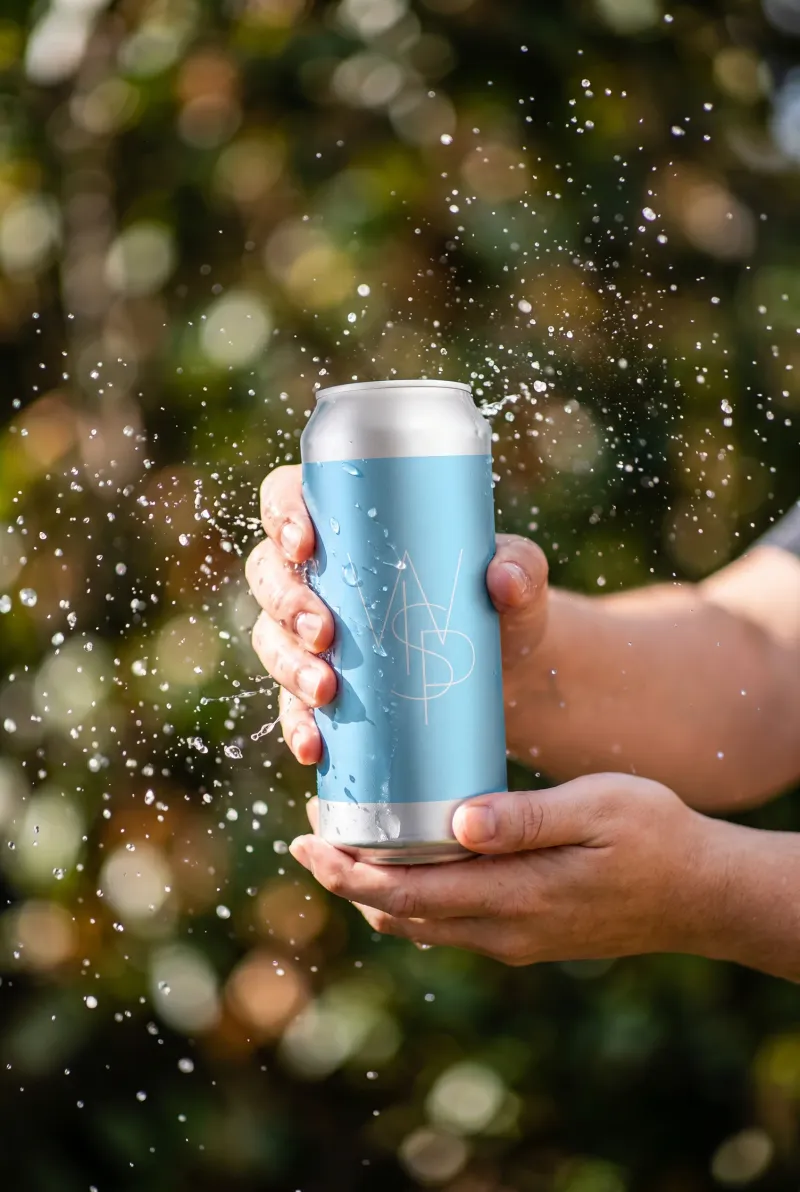 Hands holding a WSP craft beer can with a water splash against green foliage, beer lifestyle photography